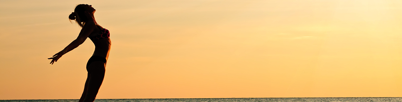 Frau reckt sich am Strand in einer Yogapose der untergehenden Sonne entgegen